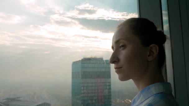 Pensive woman looking at cityscape through window of skyscraper — Stock Video