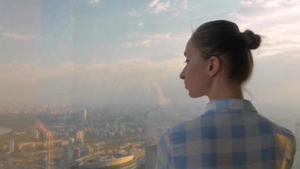 Mujer mirando paisaje urbano a través de la ventana del rascacielos - vista trasera — Vídeos de Stock