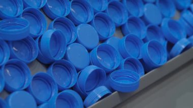 Yakın çekim: birçok mavi plastik şişe kapağı taşıma bandı üzerinde hareket ediyor, üretim hattı
