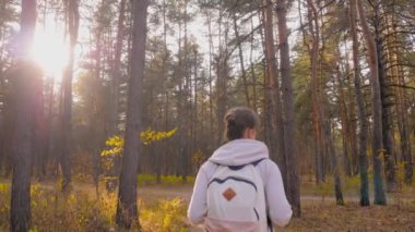 Sırt çantalı bir kadın sonbahar parkında yürüyor. Sabit çekim, güneş mercekleri parlıyor.