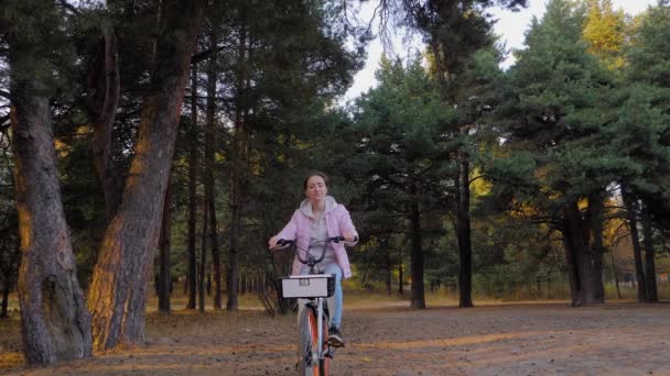 Slow motion: jonge vrouw fietsen in de herfst naaldbos bij zonsondergang — Stockvideo