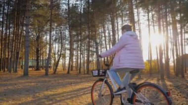 Yavaş çekim: Sonbahar şehir parkında gün batımında bisiklet süren genç bir kadın.