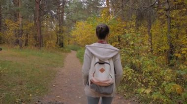 Sırt çantalı genç bir kadının sonbahar parkında yürüyüşünün arka görüntüsü.