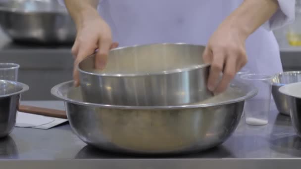 Бейкер просіює борошно під час сидіння в сталевій мисці в пекарні: закрити вгору — стокове відео