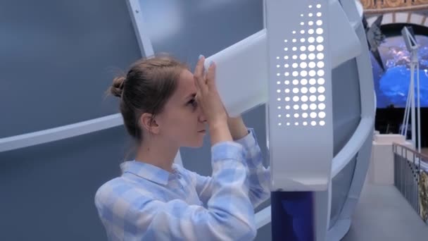 Genç bir kadın beyaz teleskoptan bakıyor ve sergiyi keşfediyor. — Stok video