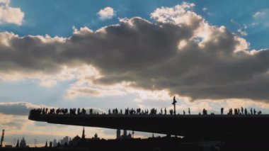 Dramatik gökyüzüne karşı yüzen yaya köprüsünde yürüyen siluetler