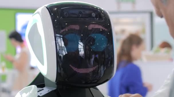 Biały ładny robot z wyświetlaczem twarz rozmawia z ludźmi na wystawie technologii — Wideo stockowe