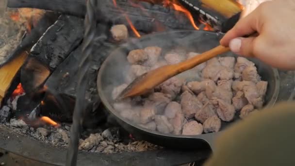 Muž se špachtlí smažící masové mísy v pánvi s otevřeným ohněm - zpomalený pohyb — Stock video