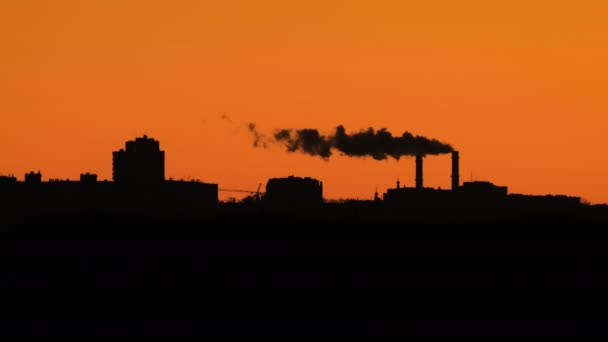 Épületek és gyári kémények sziluettjei a narancssárga ég ellen — Stock videók