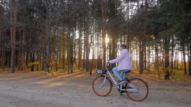 Mladá žena na kole v podzimním městském parku při západu slunce - zpomalení — Stock video