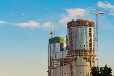 Mavi gökyüzüne karşı sarı kule vinçleri ve tamamlanmamış bina inşaatı