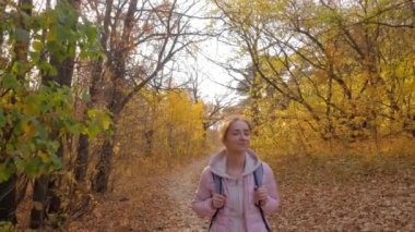 Sırt çantalı bir kadın sonbahar parkında yürüyor. Sabit çekim, güneş mercekleri parlıyor.