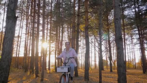 Yavaş çekim: Sonbahar şehir parkında gün batımında bisiklet süren genç bir kadın. — Stok video