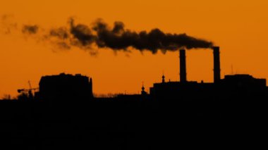 Binaların siluetleri ve turuncu gökyüzüne karşı fabrika bacaları