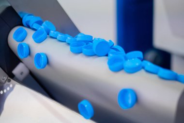 Üretim hattı - birçok mavi plastik şişe kapağı taşıma bandından düşüyor