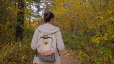 Sırt çantalı genç bir kadının sonbahar parkında yürüyüşünün arka görüntüsü.