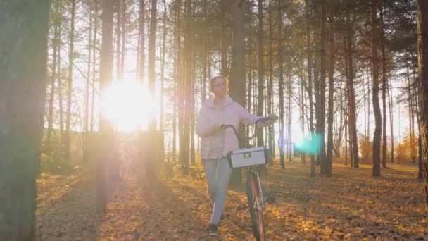 Slow motion: jonge vrouw wandelen met de fiets in de herfst stadspark - vooraanzicht — Stockvideo