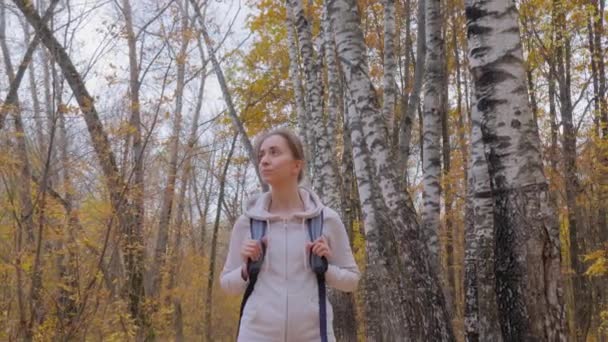 Vista frontal de la joven con mochila caminando en el parque de otoño - steadicam shot — Vídeo de stock