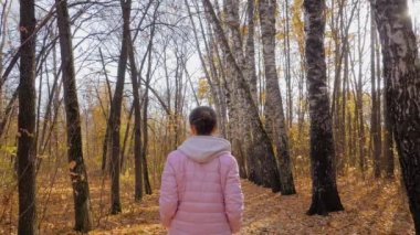 Yavaş çekim: Sonbahar parkında yürüyen genç bir kadın, sabit çekim, güneş mercekleri parlıyor
