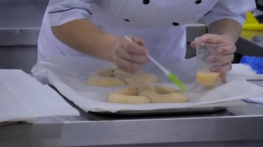 Fırıncı elleri at kuyruğu ekmeği için taze hamura sıvı yumurta uyguluyor. Yakın çekim.