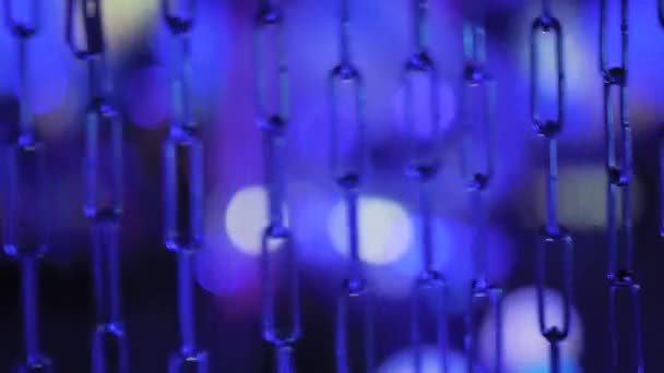 Κοντινό πλάνο - μπλε μεταλλική αλυσίδα ταλάντευση κατά πολύχρωμο φόντο bokeh — Αρχείο Βίντεο