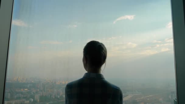 Пенсионерка смотрит на город из окна небоскреба - вид сзади — стоковое видео