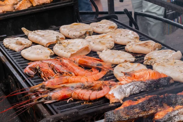 Process of cooking red langoustine shrimps, squids, salmon steaks on grill