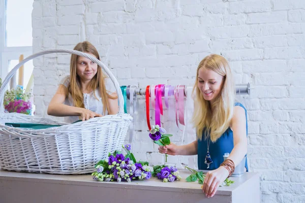 Two women florists making large floral basket with flowers in bright room