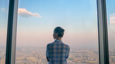 Düşünceli bir kadının gökdelen penceresinden şehir manzarasına bakışı