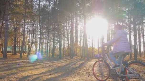 Νεαρή γυναίκα ιππασία ποδήλατο στο πάρκο της πόλης το φθινόπωρο στο ηλιοβασίλεμα - αργή κίνηση — Αρχείο Βίντεο