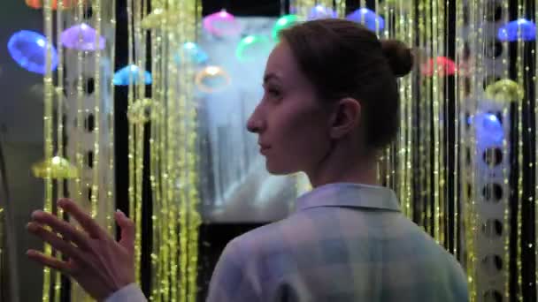 Жінка торкається світлодіодної гірлянди в темній кімнаті на захоплюючій виставці — стокове відео