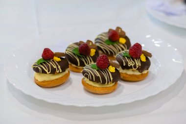 Taze, kısa hamurlu, çikolatalı tart kekleri ve beyaz tabakta meyveler satılıyor.