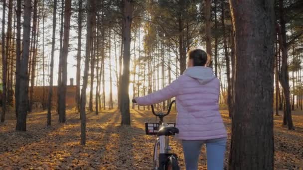Молода жінка, що йде з велосипедом в осінній хвойний ліс повільний рух — стокове відео