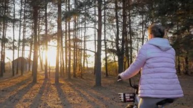 Sonbahar parkında gün batımında bisiklete binen genç bir kadın. Ağır çekim.