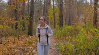 Sırt çantalı genç bir kadının sonbahar parkında yürüyüşünün ön görüntüsü.