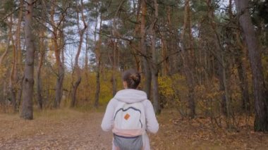 Sırt çantalı genç bir kadının sonbahar parkında yürüyüşünün arka görüntüsü.