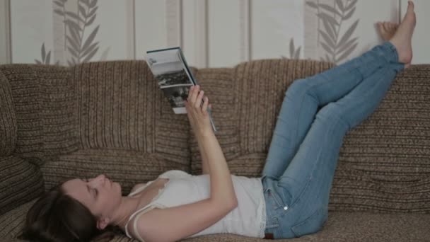 Junge Frau liest ein Buch auf der Couch — Stockvideo