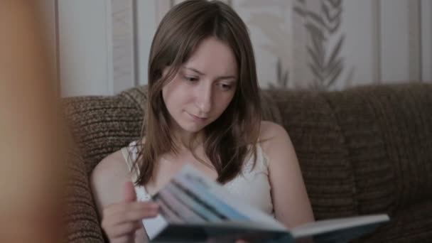 Молодая женщина читает книгу на диване — стоковое видео