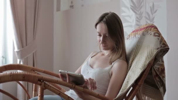 Жінка вдома розслабляється в кріслі, кріслі і використовує планшет — стокове відео