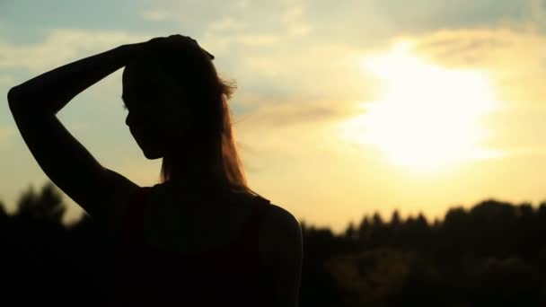 Bir kadının saçını dokunmadan bir günbatımı üzerinde bir siluet — Stok video