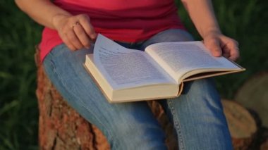 Parkta oturmuş kitap okuyan genç bir kadın.