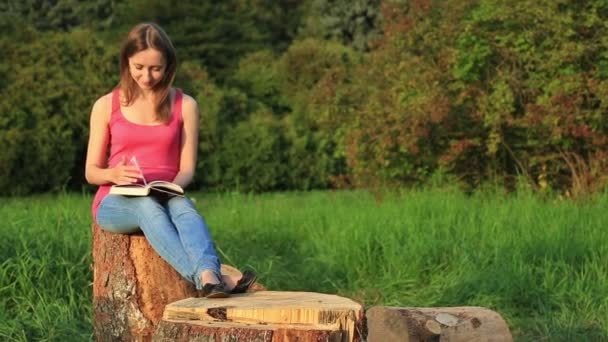 Mladá žena sedí v parku a čte si knihu — Stock video