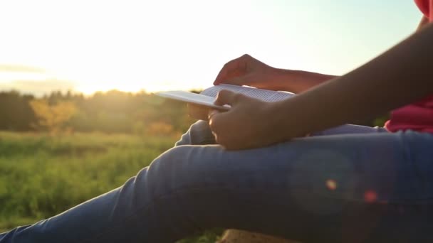 Ung kvinna som sitter i en park och läser en bok — Stockvideo