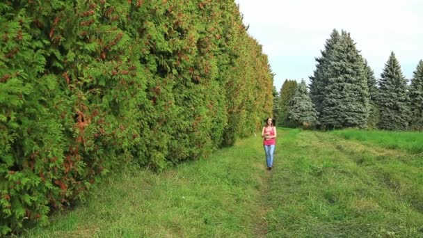 Дівчина йде через зелену алею з книгою — стокове відео