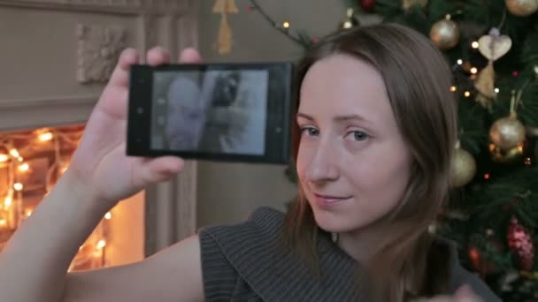 Joven mujer bonita tomando selfie en casa mientras está sentado cerca del árbol de Navidad — Vídeo de stock