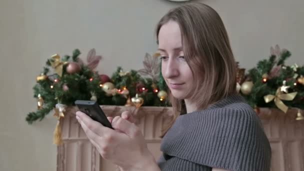 Vrouw met behulp van haar mobiele telefoon met Kerstmis thuis in de woonkamer — Stockvideo
