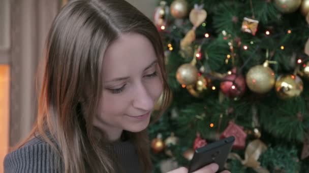 Mujer usando su teléfono móvil en Navidad en casa en la sala de estar — Vídeos de Stock