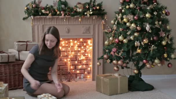 Молодая женщина кладет подарки под елку — стоковое видео