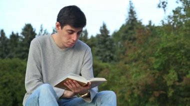 Genç adam bir parkta oturan ve bir kitap okuma