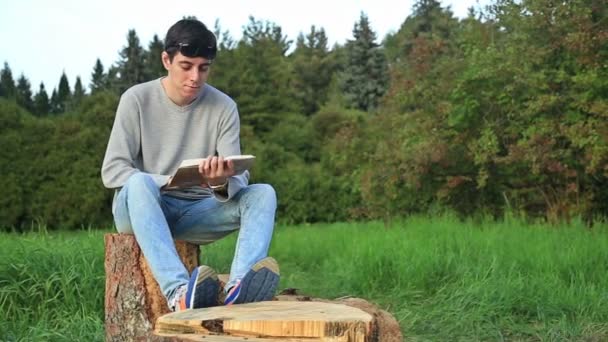 Jonge man zit in een park en het lezen van een boek — Stockvideo